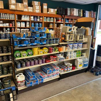Shelves filled with various paint cans, brushes, and supplies in a store. Products are neatly organized, creating a vibrant and colorful display.